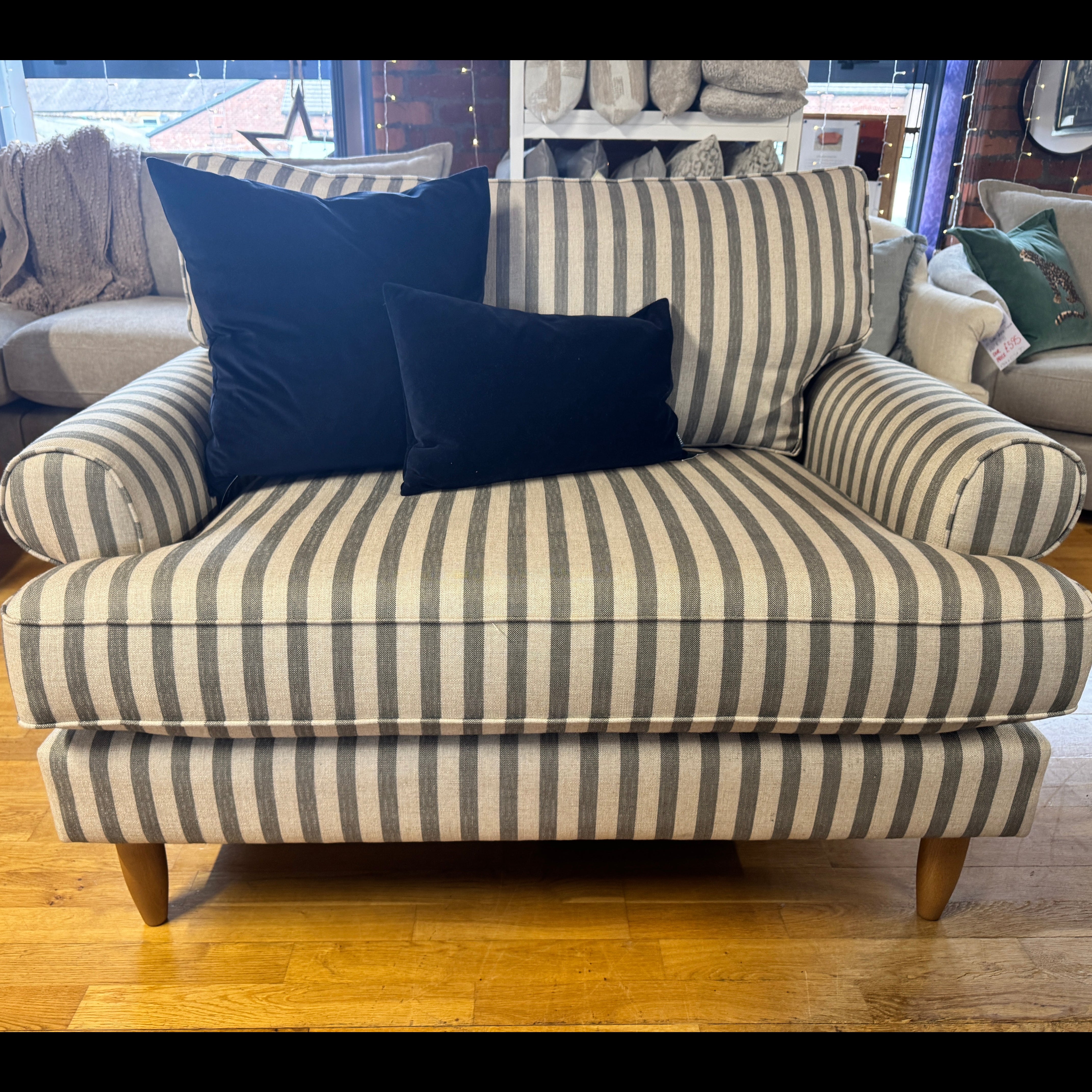 A striped armchair with beige and gray vertical stripes, styled with two dark blue velvet pillows,